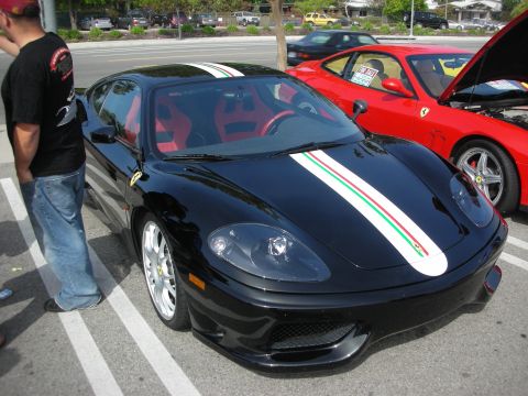 1998 Ford Crown Victoria - Front three-quarter view of a black Ferrari coupe with an Italian-flag racing stripe and red interior beside a red Ferrari.