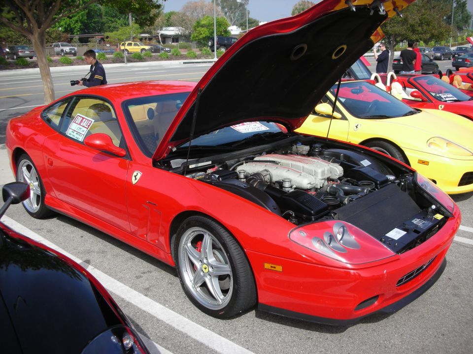 Red Ferrari coupe with hood open showing V12 engine at a show
