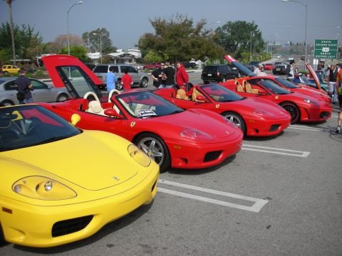 1998 Ford Crown Victoria - line of Ferrari convertibles, one yellow and several red, parked side by side with spectators at an outdoor car show.