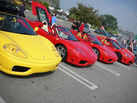 1998 Ford Crown Victoria - Front-angle view of one yellow and three red Ferrari convertibles parked in a row on a sunny show field.