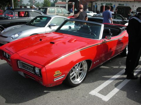 1998 Ford Crown Victoria - Side view of a red Pontiac GTO 'The Judge' convertible with gold stripe and chrome wheels parked among show cars.