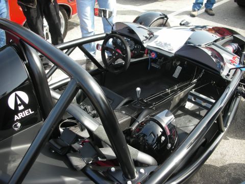 1998 Ford Crown Victoria - Interior of a black Ariel Atom exoskeleton car showing the bare cockpit, racing seat, steering wheel and a helmet.