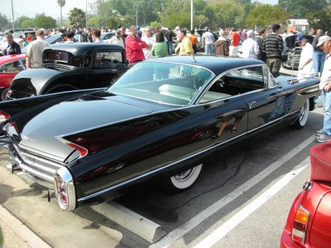 1998 Ford Crown Victoria - black early-1960s Cadillac hardtop with tailfins and whitewall tires among a crowd at a car show.
