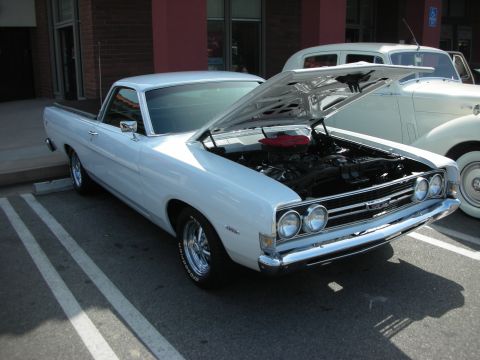 1998 Ford Crown Victoria - white Ford Ranchero car-based pickup with its hood raised to show the engine, parked by a building.