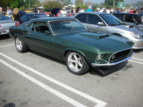 1998 Ford Crown Victoria - dark green 1969-style Ford Mustang fastback with chrome wheels parked at a crowded car show.