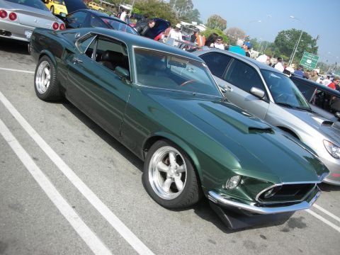 1998 Ford Crown Victoria - Front-quarter view of a dark green Ford Mustang fastback with polished five-spoke wheels at a show.