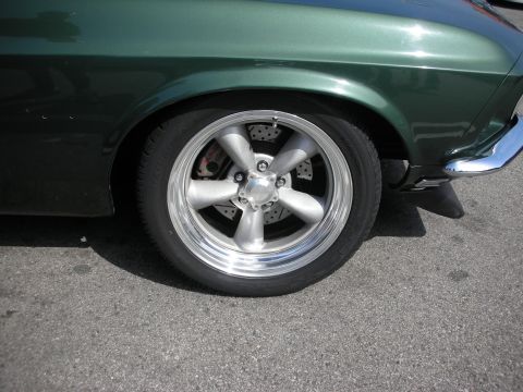 1998 Ford Crown Victoria - Close-up of a polished five-spoke wheel and disc brake on a dark green car.