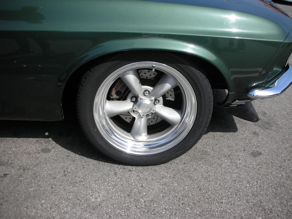 Polished five-spoke wheel on green car with disc brake
