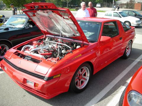 1998 Ford Crown Victoria - red 1980s Chrysler Conquest/Mitsubishi Starion with hood raised exposing a turbocharged engine.