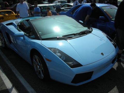 1998 Ford Crown Victoria - light blue Lamborghini Gallardo shown front-on at a sunny car meet, parked among other sports cars and onlookers.