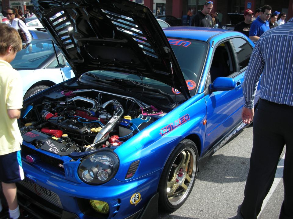 Blue Subaru Impreza WRX sedan with open hood and Falken decals at a car show