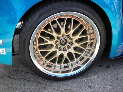 1998 Ford Crown Victoria - Detail of a gold multi-spoke mesh wheel with a polished lip and low-profile tire on a teal car.