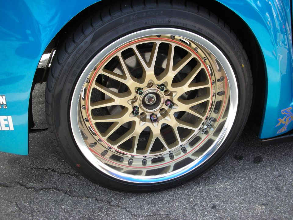 Close-up of gold mesh wheel with polished lip on a teal car