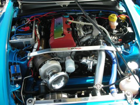 1998 Ford Crown Victoria - Engine bay of a teal car showing a red valve cover, a large turbocharger and a Cusco strut brace.