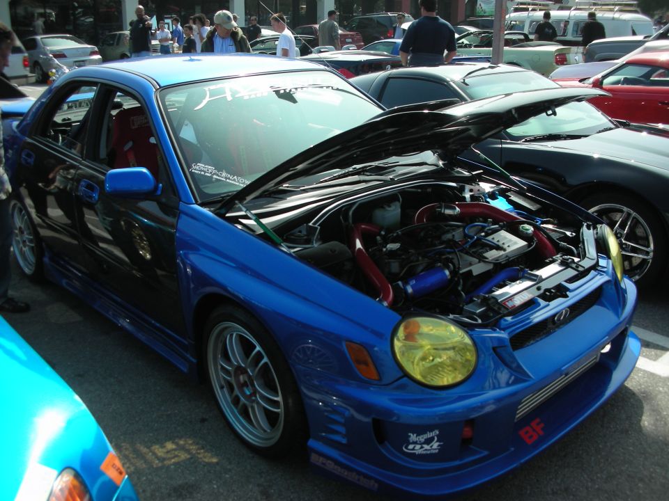 Blue Subaru Impreza WRX with open hood and yellow headlights at a car show