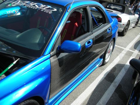 1998 Ford Crown Victoria - Profile of a blue compact sedan with a carbon-fiber door panel, blue roll cage and red racing seats visible inside, parked at an outdoor sh…