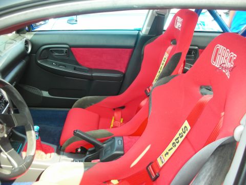 1998 Ford Crown Victoria - Interior shot of two red Sparco racing bucket seats with yellow harness straps and a blue roll cage in a gutted cabin.