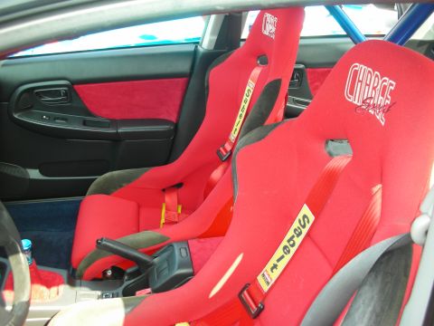 1998 Ford Crown Victoria - Two red carbon-backed Sparco racing seats with harnesses, manual shifter and blue roll cage inside a stripped interior.