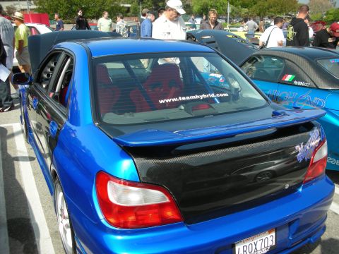 1998 Ford Crown Victoria - Rear three-quarter of a blue sedan with carbon-fiber trunk lid, spoiler and a www.teamhybrid.com rear-window banner at a car show.