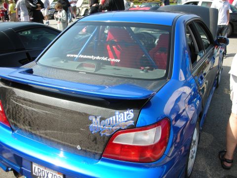 1998 Ford Crown Victoria - Rear quarter of a blue sedan with carbon-fiber trunk lid wearing Meguiar's and Team Hybrid decals, parked among show cars.