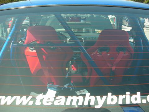 1998 Ford Crown Victoria - View through a blue car's rear glass showing red racing seats and roll cage, with a www.teamhybrid decal across the window.