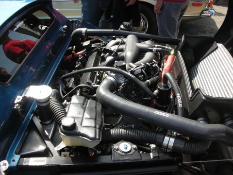 1998 Ford Crown Victoria - Detailed engine bay of a teal sports car showing intake plenum, coolant reservoir, black hoses and SPEC-branded parts.
