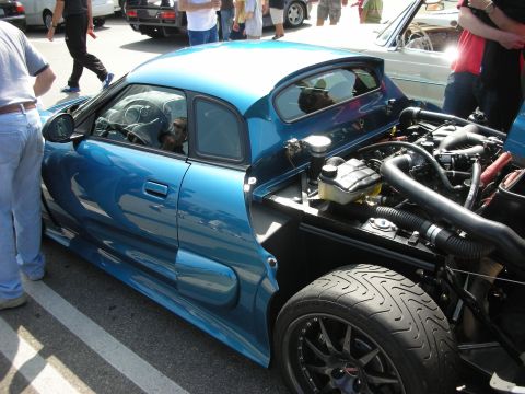1998 Ford Crown Victoria - teal mid-engine sports car with its rear engine cover open, a dog visible in the cabin, at a crowded car show.