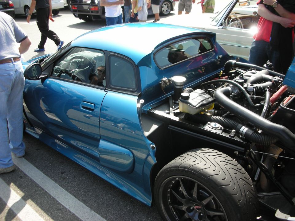 Teal mid-engine sports car with rear hatch open showing engine, dog inside