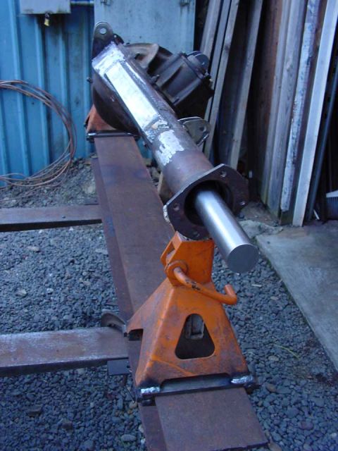 1979 Ford Bronco - A metal axle housing is supported by orange jack stands, with a silver shaft protruding from its flange.