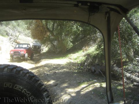 1987 Suzuki Samurai - Two off-road vehicles navigate a dusty trail through a wooded area.
