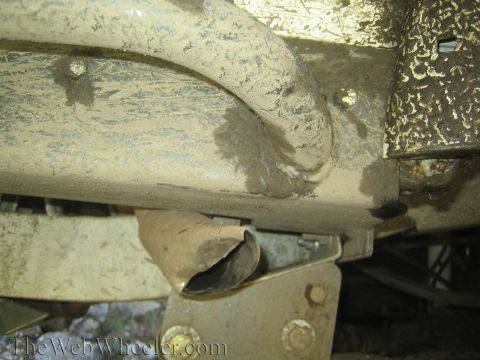1987 Suzuki Samurai - Close-up view of a damaged exhaust pipe and the underside of a vehicle's frame, covered in mud and grime.