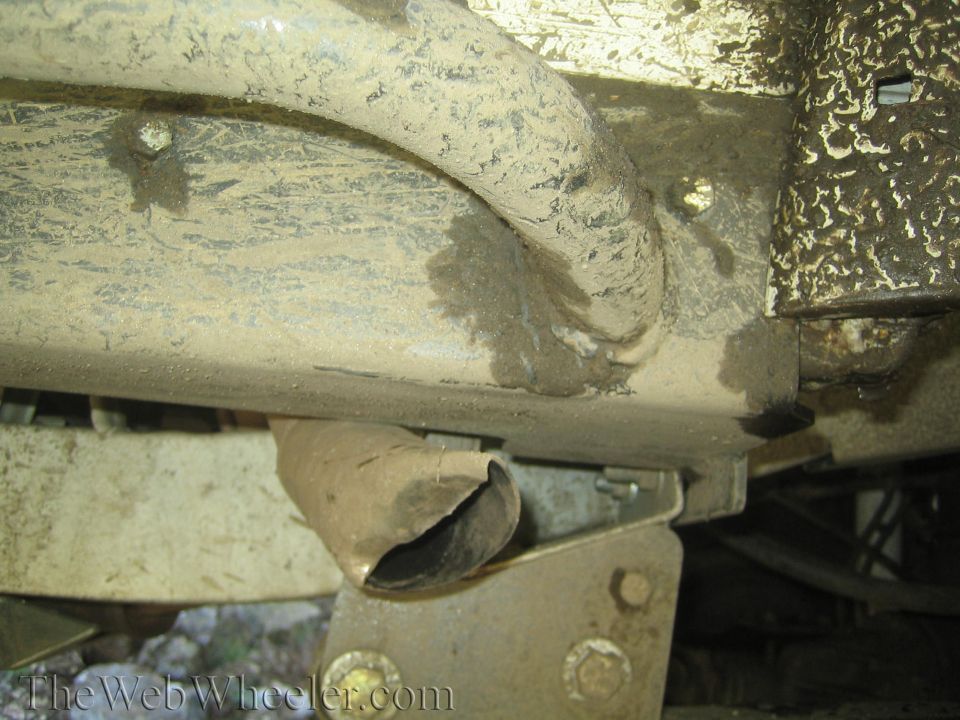 Damaged exhaust pipe on a dirty vehicle frame