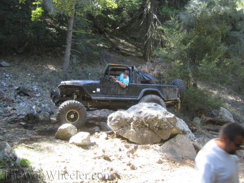 1987 Suzuki Samurai - Off-road vehicle tackling a challenging rocky path in a wooded area.
