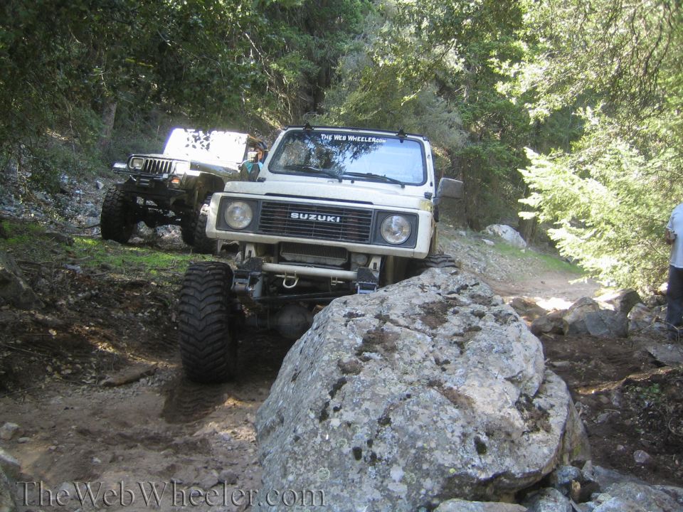 White 1987 Suzuki Samurai navigating a rocky trail with a Jeep behind it
