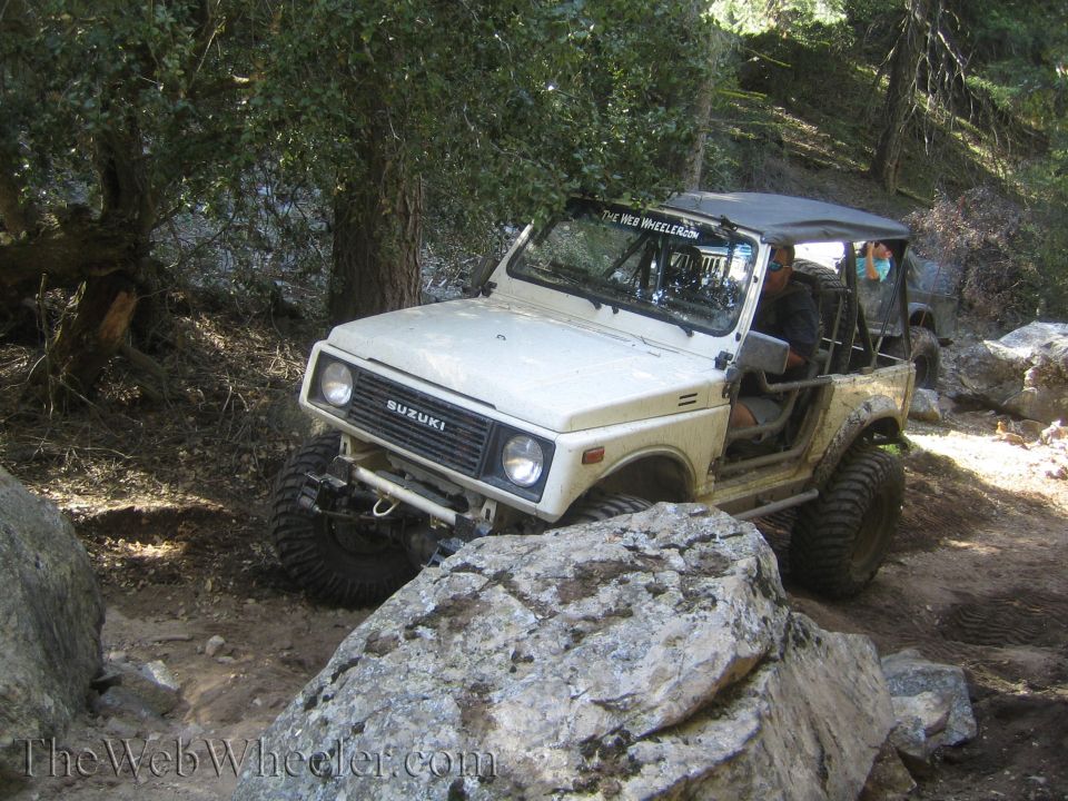 White Suzuki Samurai off-roading on a rocky trail, front 3/4 view