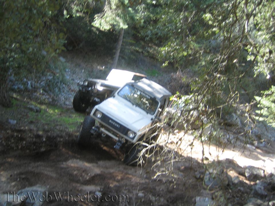 White 1987 Suzuki Samurai off-roading on a dirt trail with another vehicle behind it