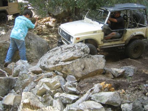 1987 Suzuki Samurai - Suzuki Samurai tackles a challenging rocky obstacle on an off-road trail. Another vehicle is present.