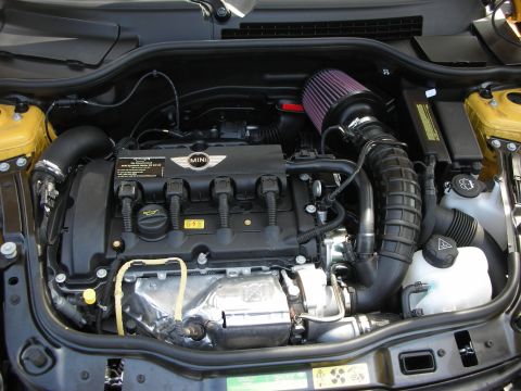 1998 Ford Crown Victoria - Engine bay of a yellow MINI showing the transverse engine, MINI-branded valve cover and a red cone intake filter.