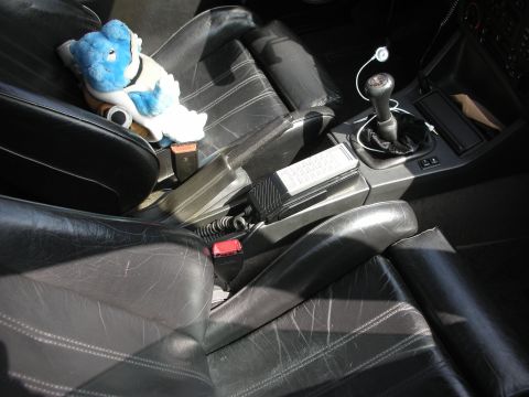 1998 Ford Crown Victoria - Black leather car interior with worn seats, a manual shifter and a blue Smurf plush figure resting on the passenger seat.