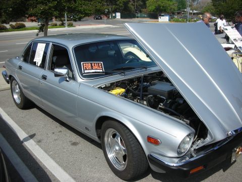 1998 Ford Crown Victoria - Silver four-door Jaguar XJ sedan with its hood raised and FOR SALE signs in the windows, parked at a roadside car show.