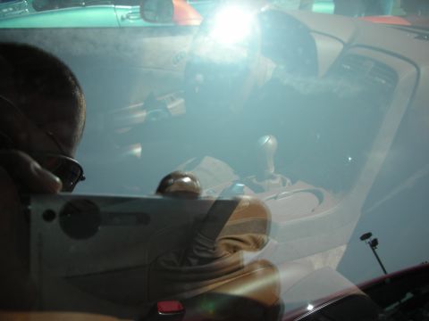 1998 Ford Crown Victoria - Glare-filled shot through a windshield showing the interior of a sports car with a manual gear shifter, photographer reflected in glass.
