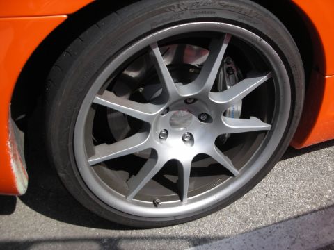 1998 Ford Crown Victoria - Detail of a gray ten-spoke alloy wheel and low-profile tire on an orange sports car parked on pavement.