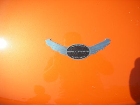 1998 Ford Crown Victoria - Close-up of a winged metal Callaway emblem reading Powerfully Engineered mounted on glossy orange bodywork.