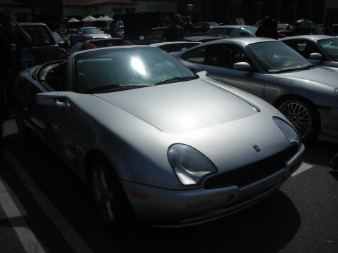 1998 Ford Crown Victoria - Front three-quarter view of a silver convertible sports car with oval headlights parked among other cars at a show.