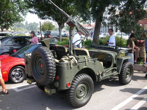 1998 Ford Crown Victoria - Rear view of an olive-drab military Jeep fitted with a roof-mounted machine gun and spare tire, displayed at an outdoor show.