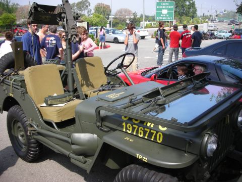 1998 Ford Crown Victoria - Side view of an olive-drab military Jeep marked USMC 1976770 with a mounted gun, parked beside a red sports car.