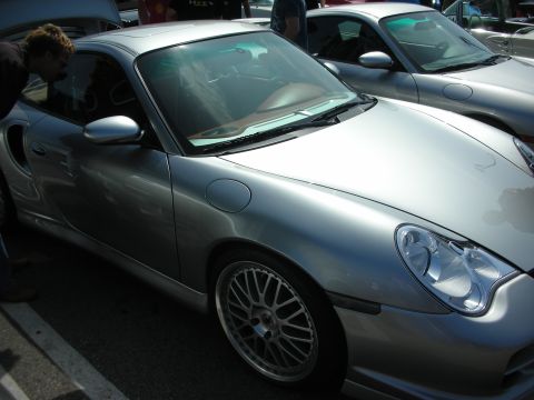 1998 Ford Crown Victoria - Front side view of a silver Porsche 911 with multi-spoke wheels, a person leaning toward its window at a car show.