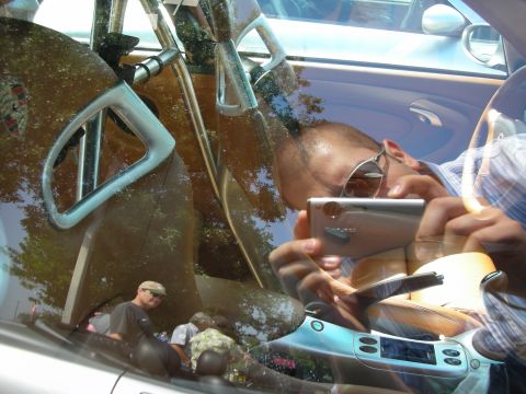 1998 Ford Crown Victoria - Through a glare-heavy car window, a roll cage and tan interior are visible alongside the reflected photographer holding a camera.