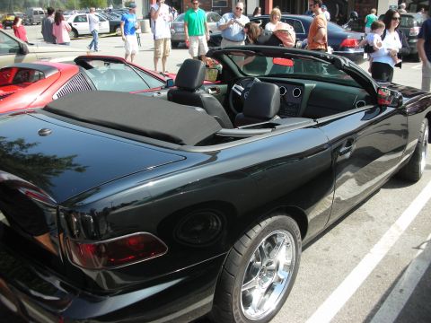 1998 Ford Crown Victoria - black custom convertible with its top folded down sits in a crowded car-show parking lot, showing twin chrome wheels and dark leather seats.