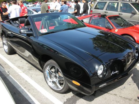 1998 Ford Crown Victoria - glossy black Avanti convertible with chrome wheels parked at a car show, a red Ferrari with its hood up visible behind it.